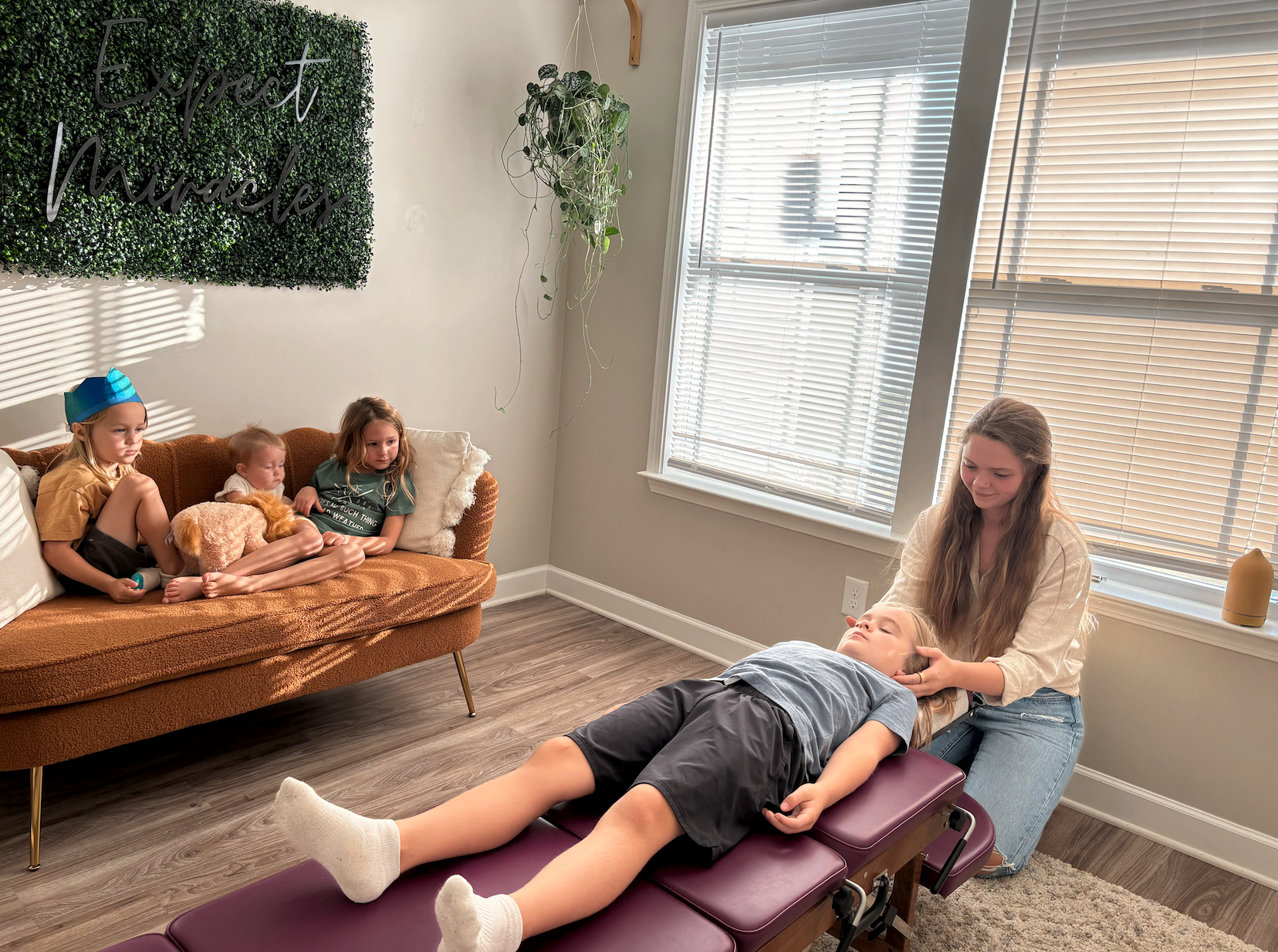 Dr. Shannon adjusting a child in the office while siblings relax on the couch nearby